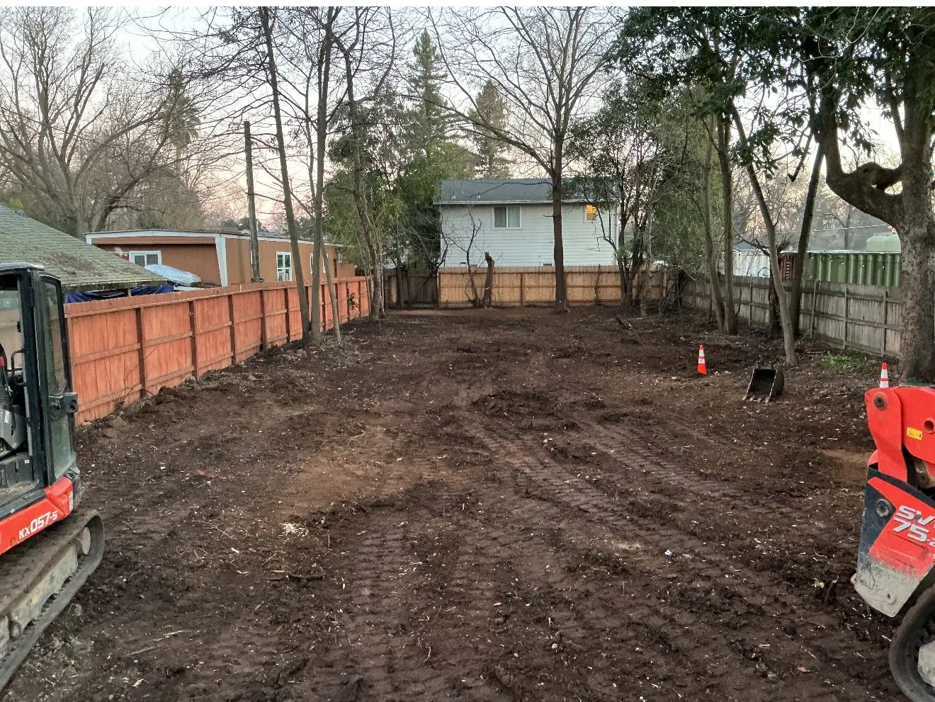 Cleared dirt lot between wood fences with a skid steer at the far end