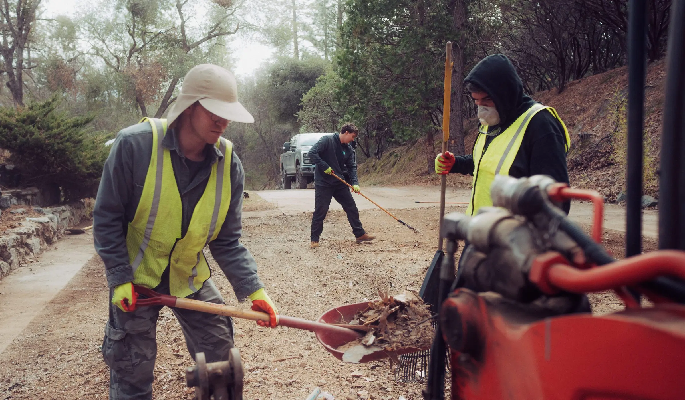 Two crew members raking and shoveling debris on a gravel driveway