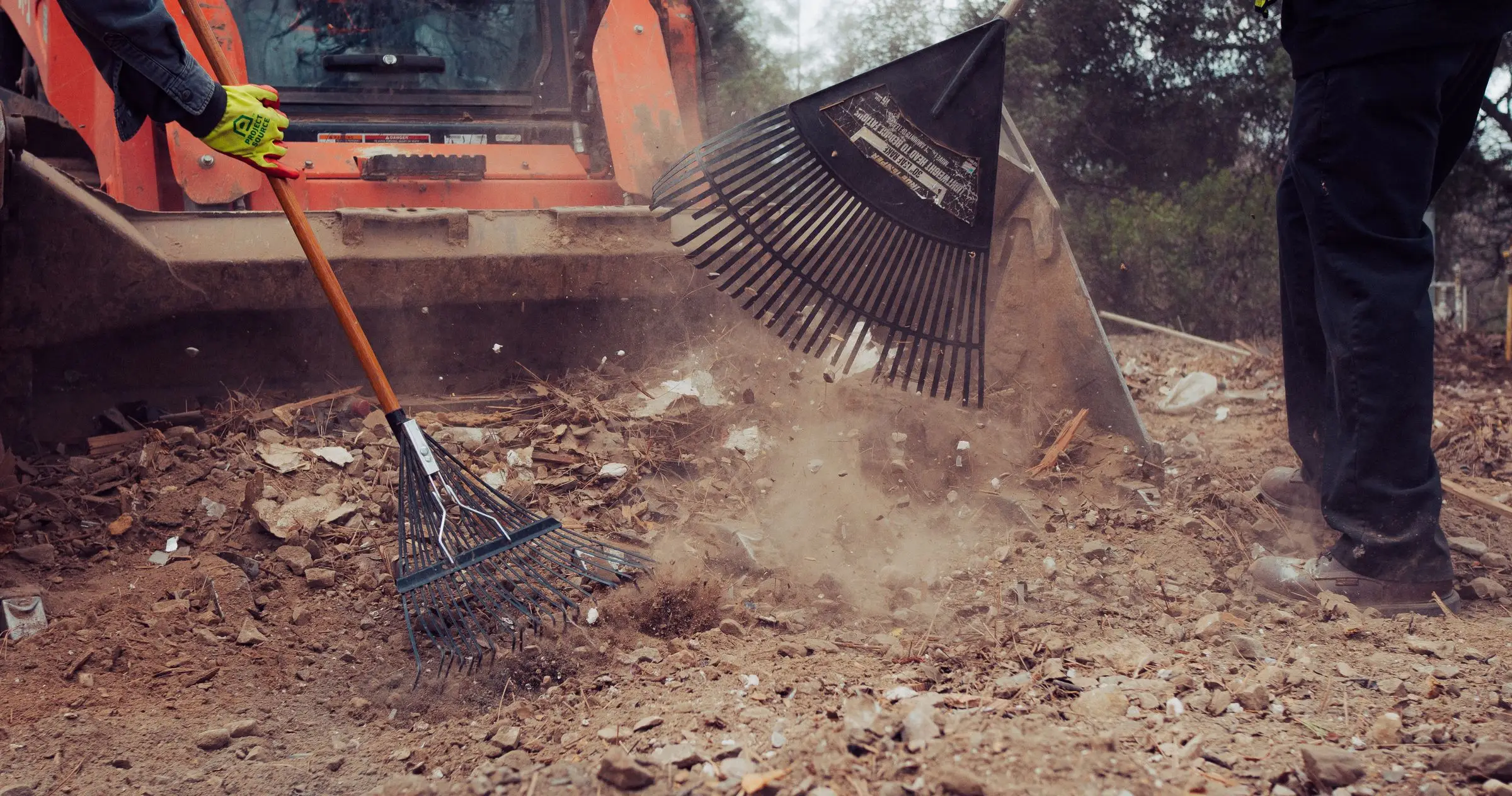 Crew member raking debris toward a skid steer bucket