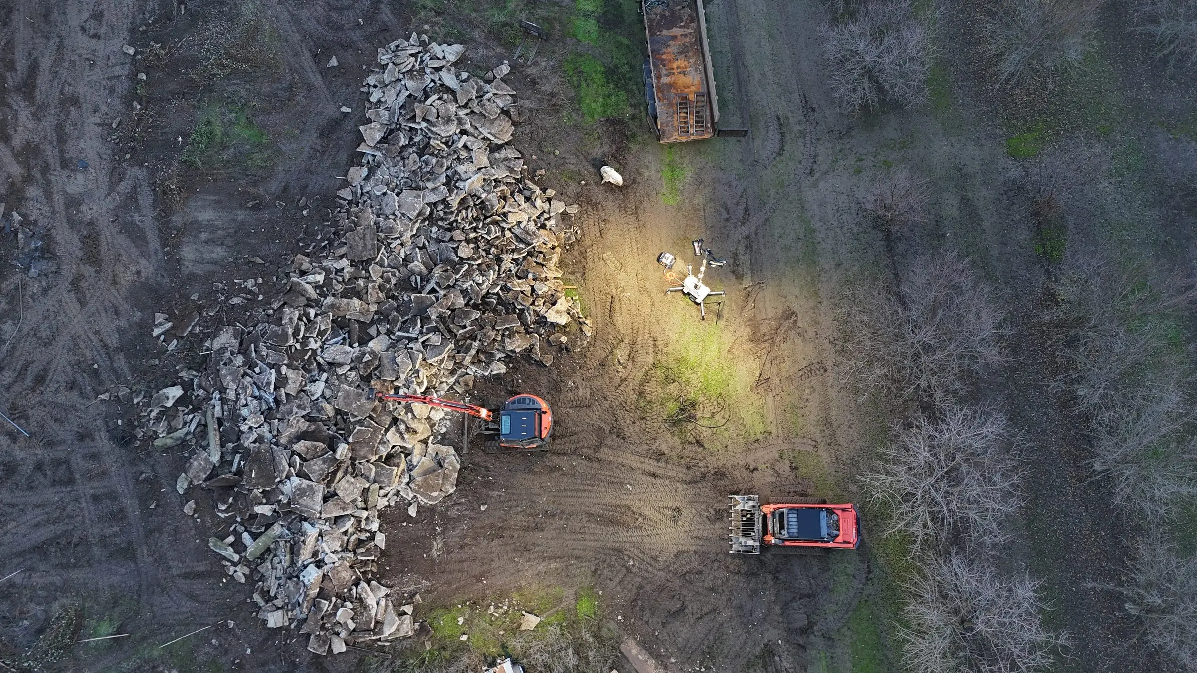 Aerial view of a large pile of broken concrete in an orchard with an excavator and skid steer