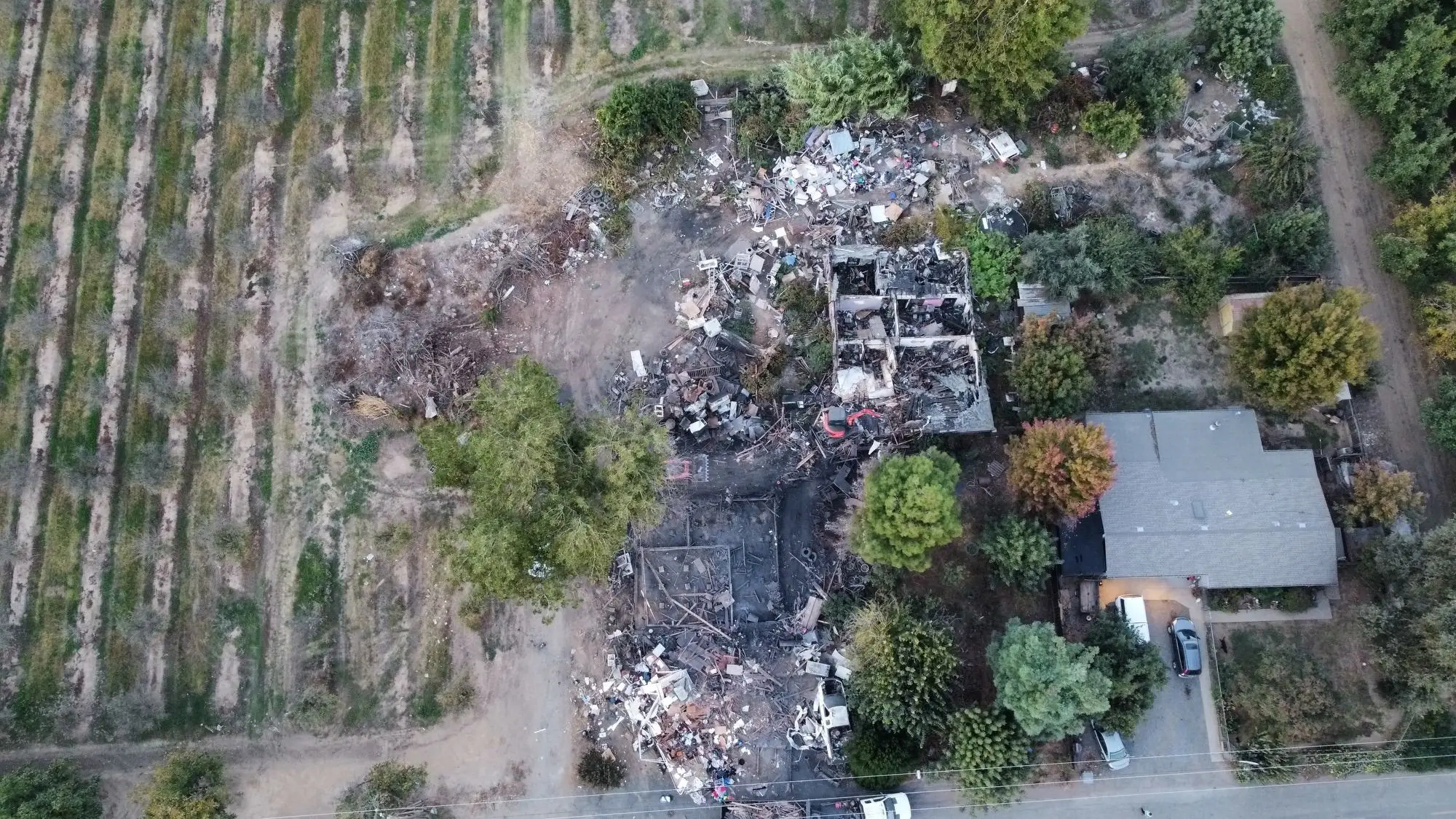 Aerial view of burned structures and debris beside an orchard