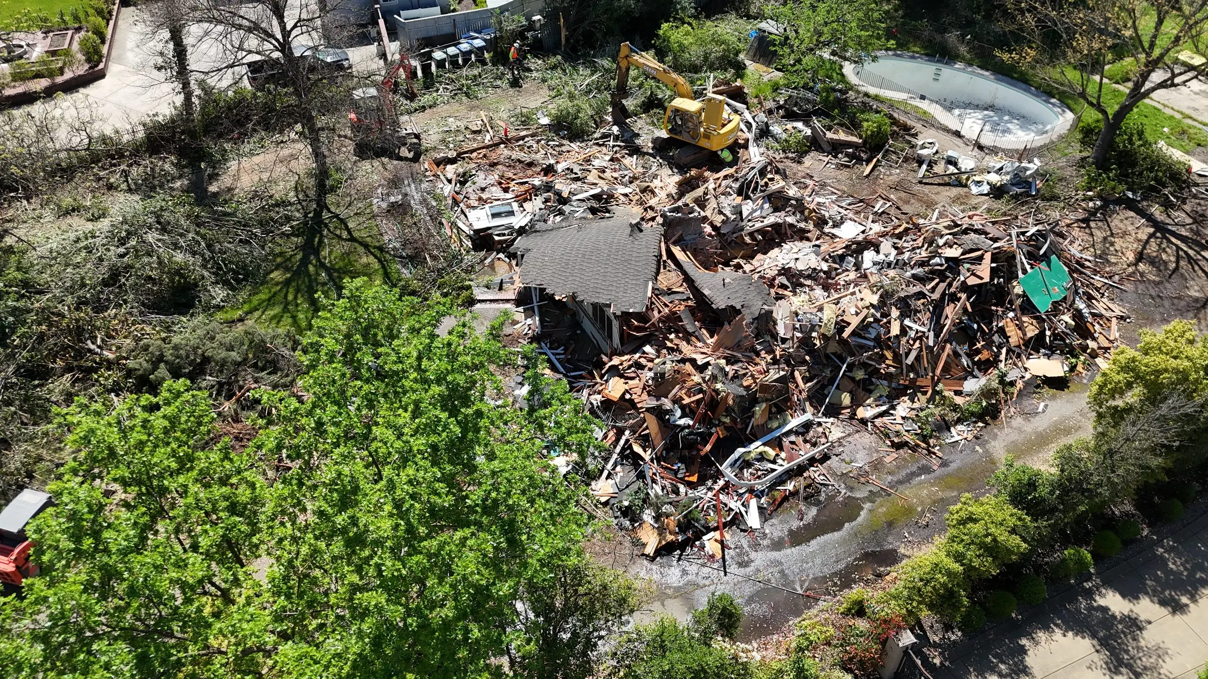 Aerial view of a house demolition debris pile next to a backyard pool