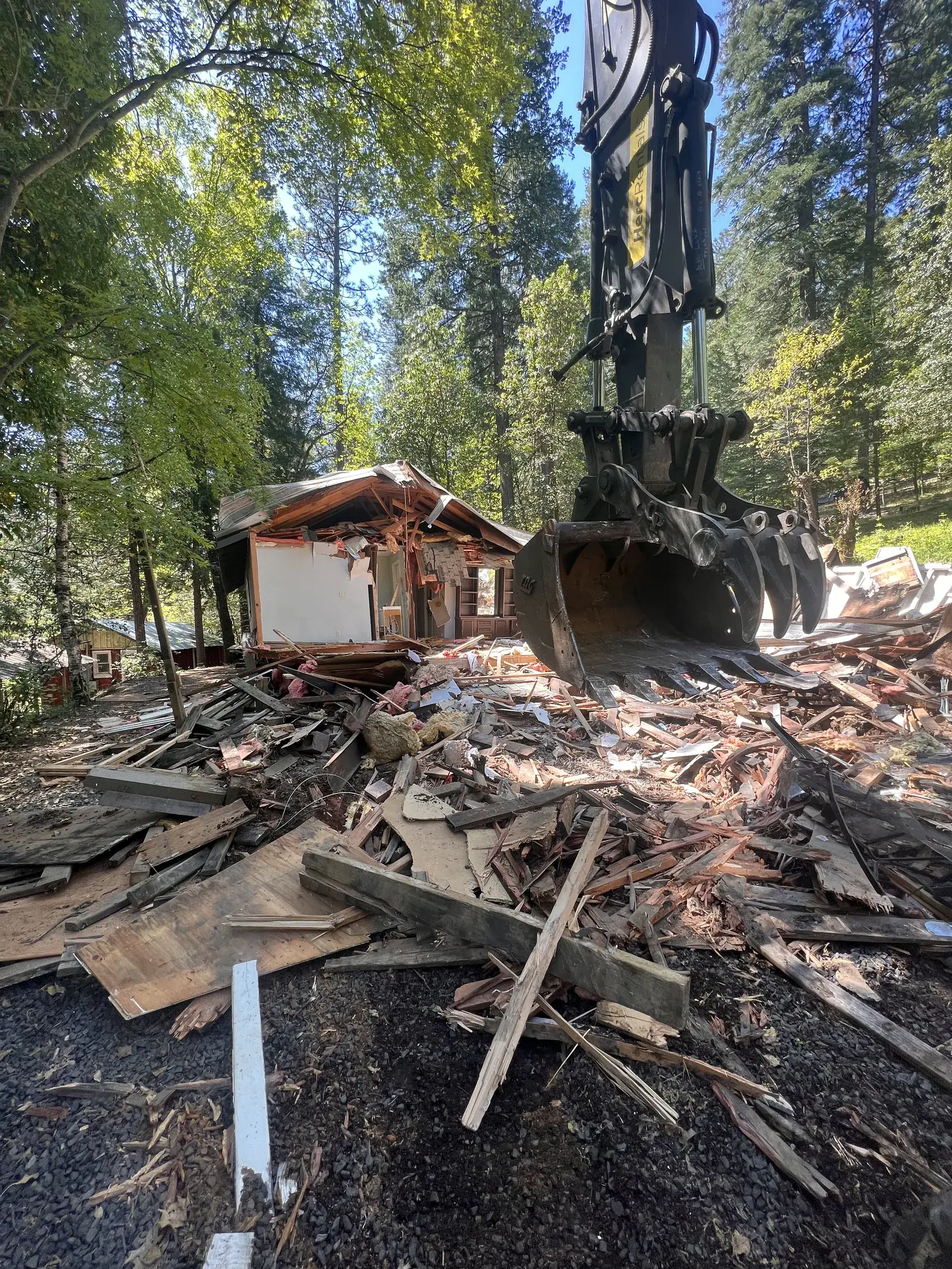 Excavator grapple mid-demolition with debris field in Magalia