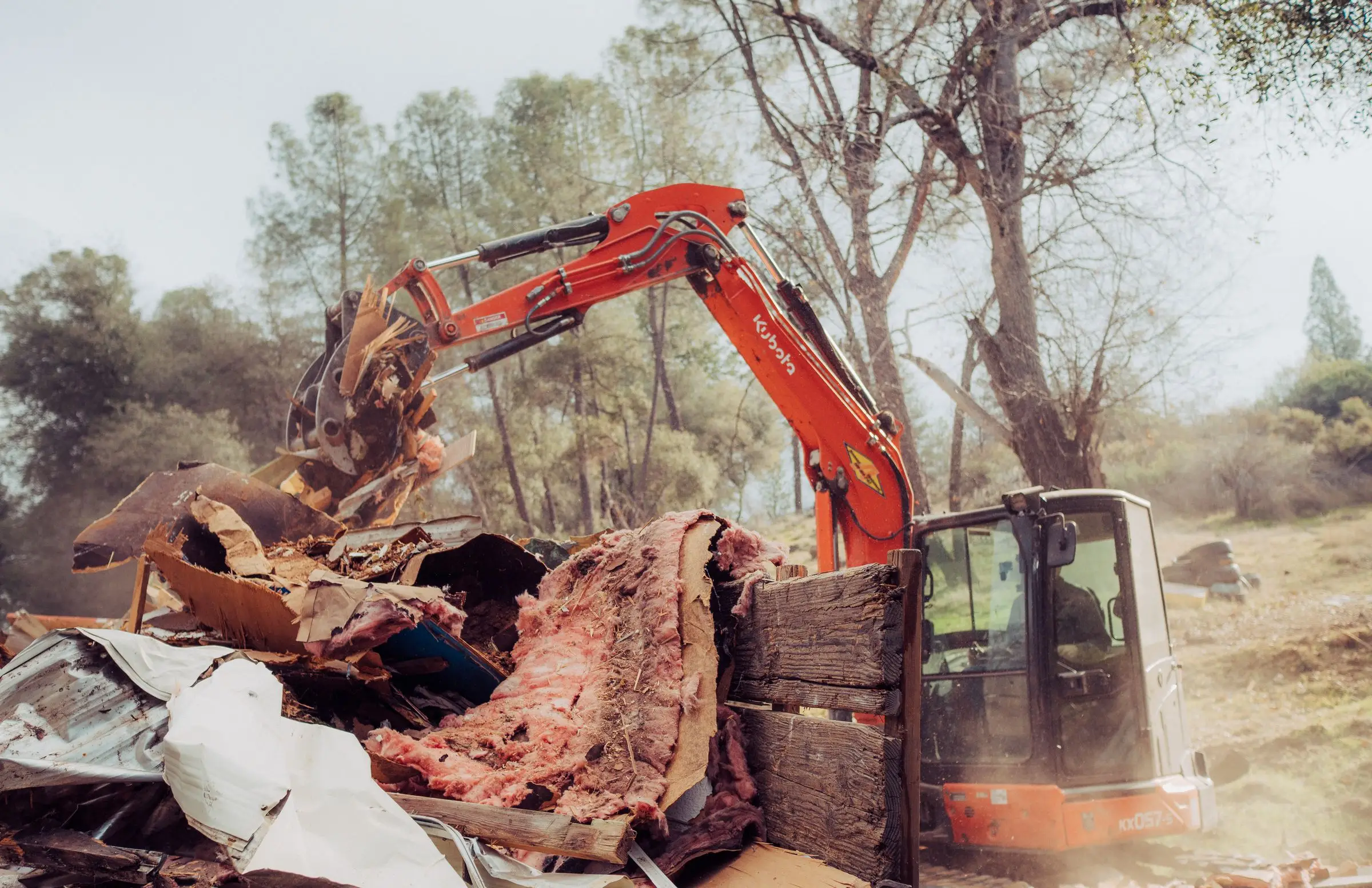 Excavator grapple loading mobile home debris and insulation