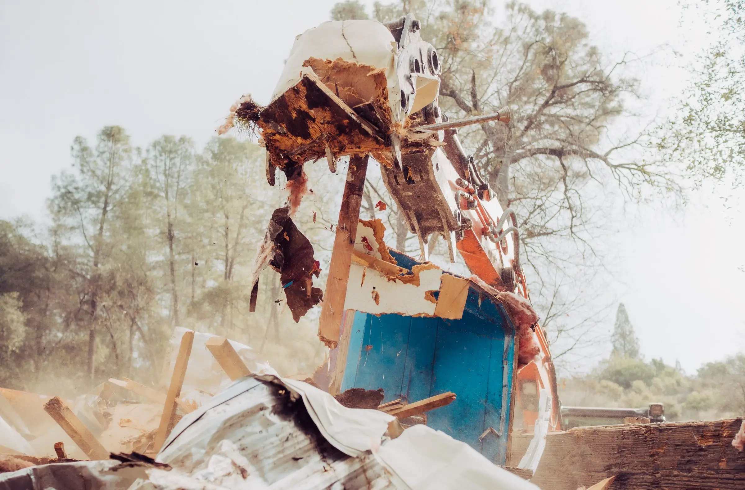 Excavator grapple lifting a broken section of mobile home wall