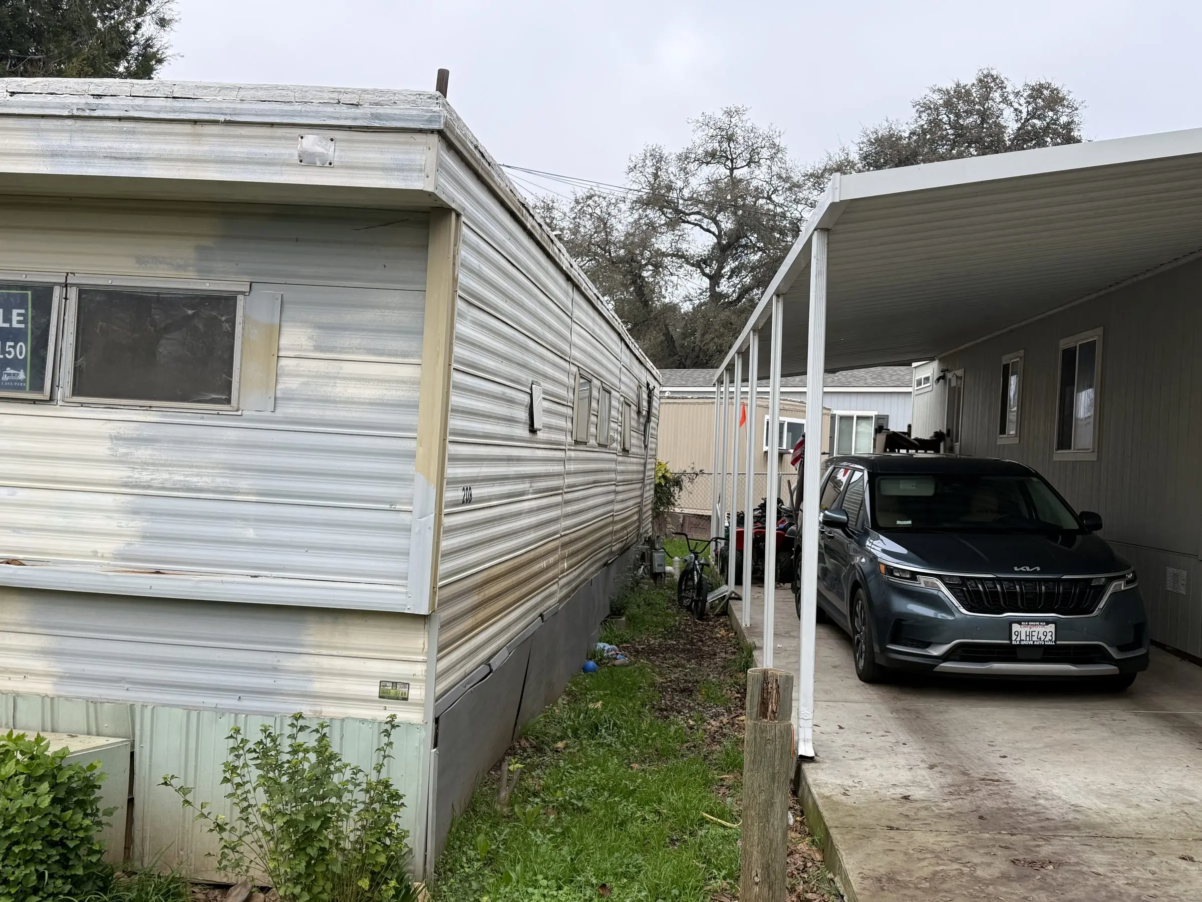 Older mobile home with metal siding next to a neighbor's carport
