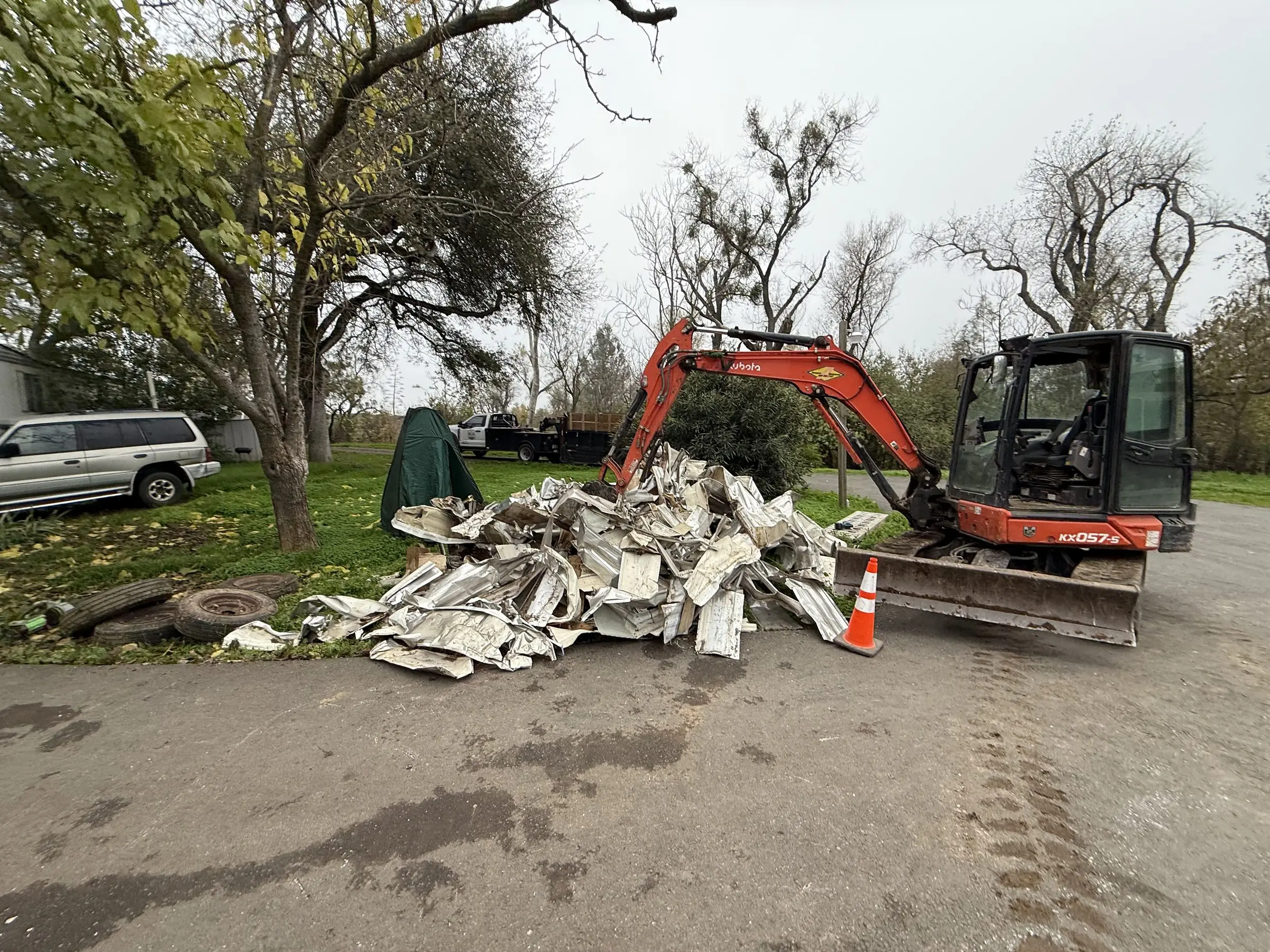 Excavator beside a pile of mobile home siding and debris