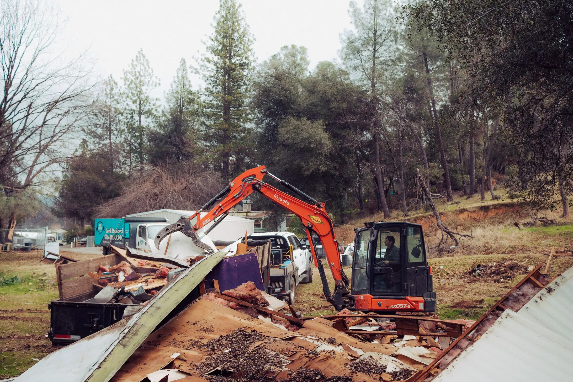 Excavator tearing down a mobile home, with debris in the foreground