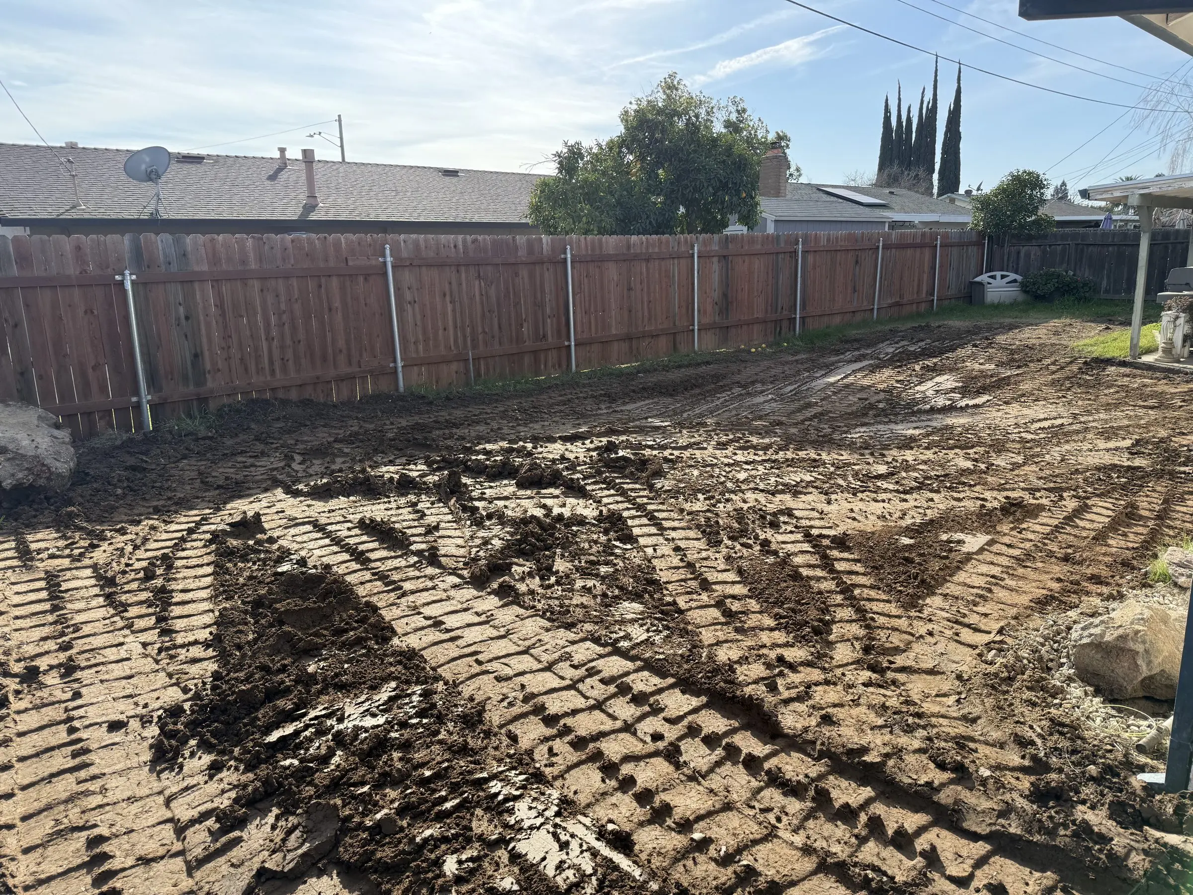Backyard where a pool was filled and compacted, with equipment tracks in the soil