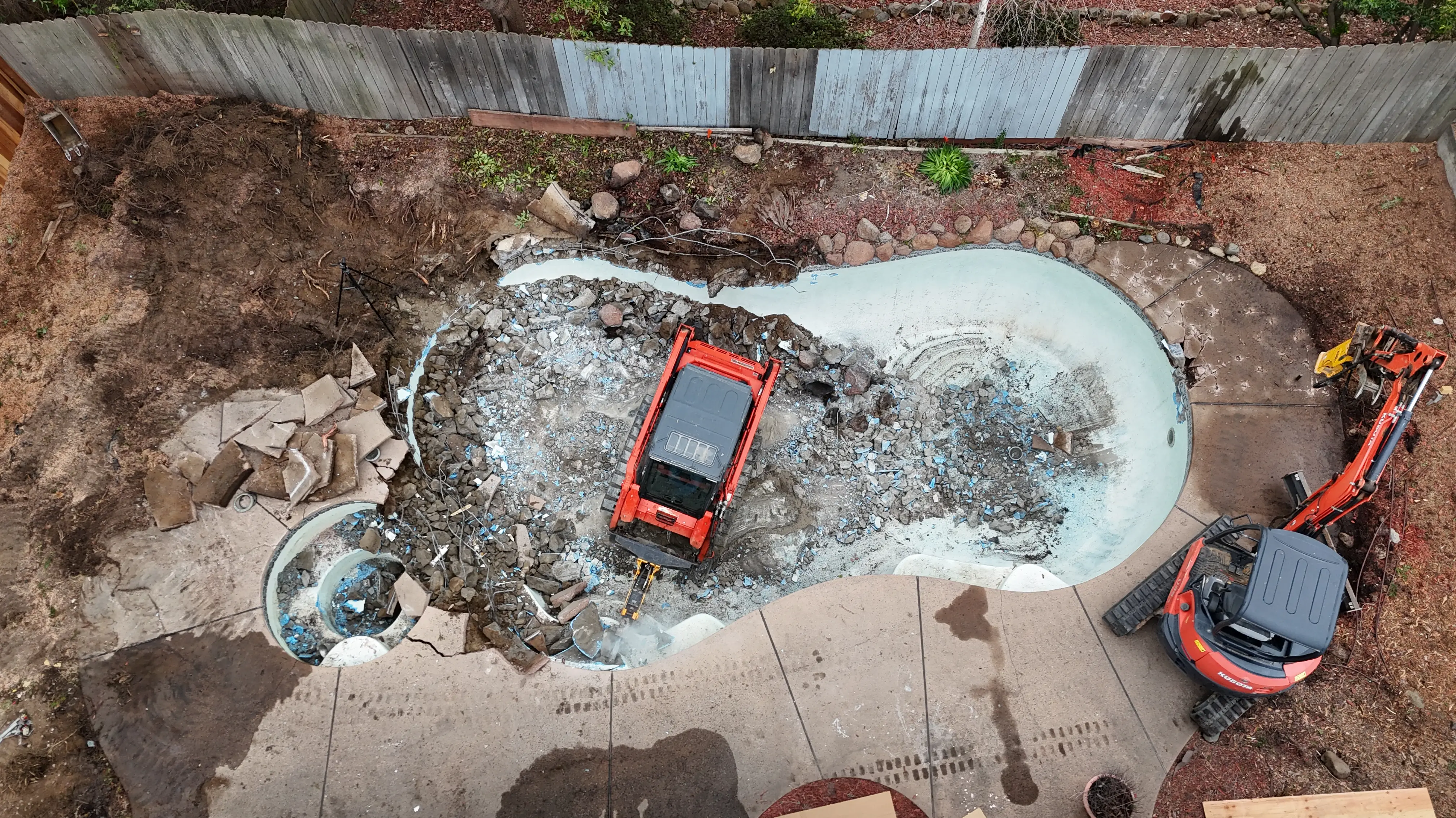 Aerial view of a backyard pool being demolished with a skid steer and mini excavator